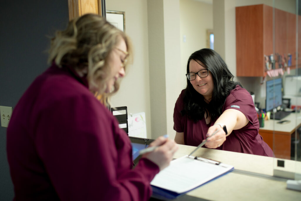 woman at a counter pointing to a paper that another woman is filling out at Desert Valley Oral Surgery