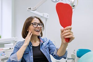 woman holding a mirror and smiling at her dental work